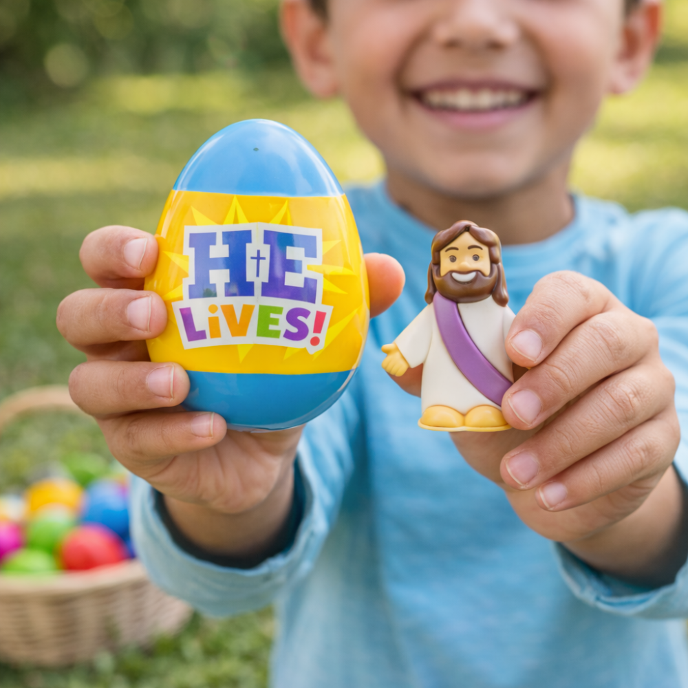 Child holding a colorful Easter egg with 'He Lives!' and a Jesus figurine outdoors.