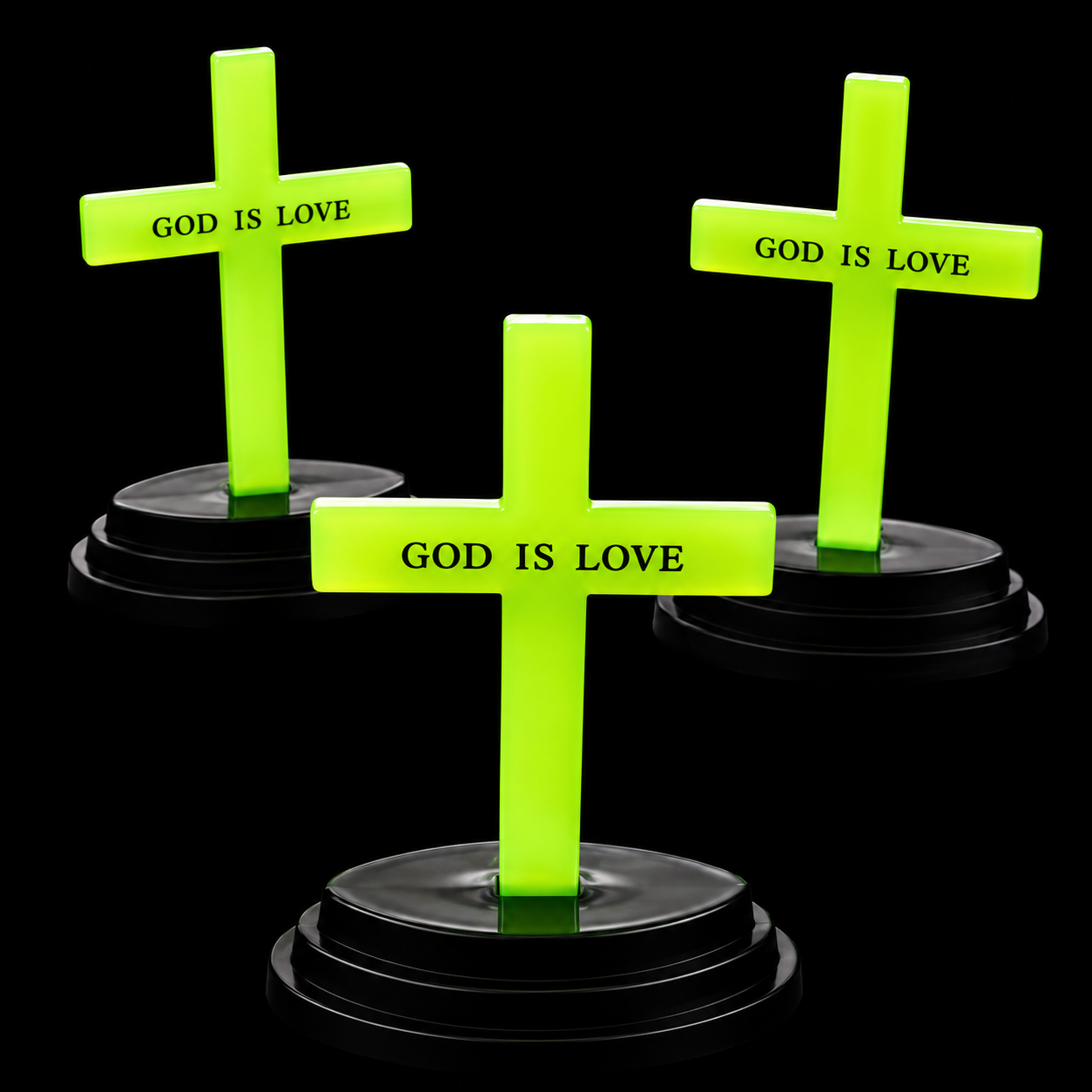 Three bright neon green cross-shaped tombstones with black bases, each printed with the words 'GOD IS LOVE' in black text, arranged on a black background.
