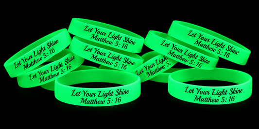 Glow-in-the-dark green silicone bracelets with “Let Your Light Shine Matthew 5:16” displayed on a black background.
