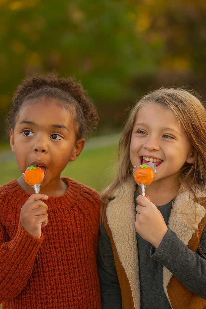 Two children eating candy corn outdoors on a blurred green background. Thanksgiving candy.