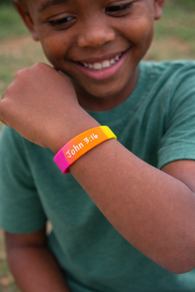 Child wearing a colorful wristband with text, Jesus loves me, outdoors.