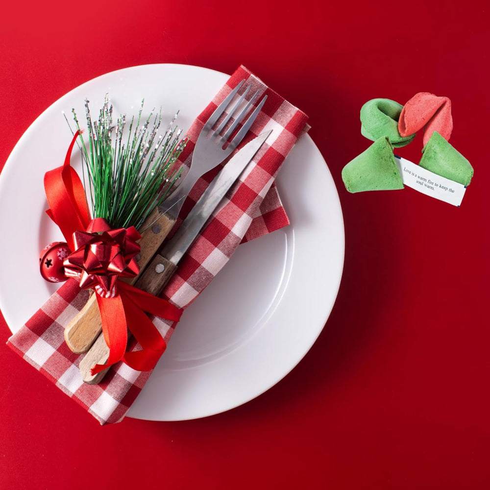 Decorative table setting with a white plate, red checkered napkin, silverware, and a small green ornament on a red background.