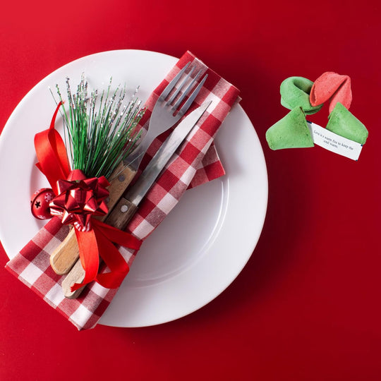 Decorative table setting with a white plate, red checkered napkin, silverware, and a small green ornament on a red background.