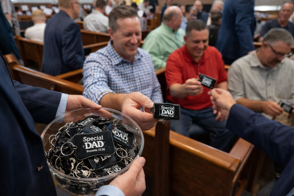 Person holding a container of 'Special Dad' keychains in a church setting.
