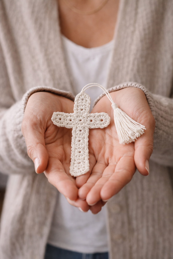 Person holding a small crocheted cross bookmark with tassel in their hands.