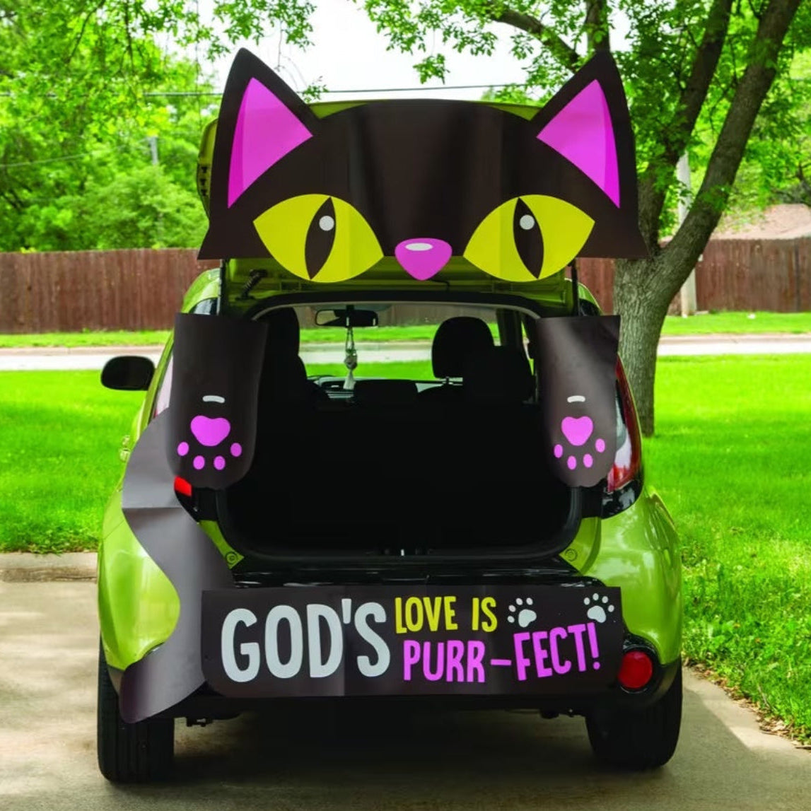 A lime green car parked outdoors on a driveway with its trunk open, decorated with a large black cat face graphic on the trunk lid area, matching cat ears on the sides, paw-print accents, and a bumper banner that reads “GOD'S LOVE IS PURR-FECT!”.