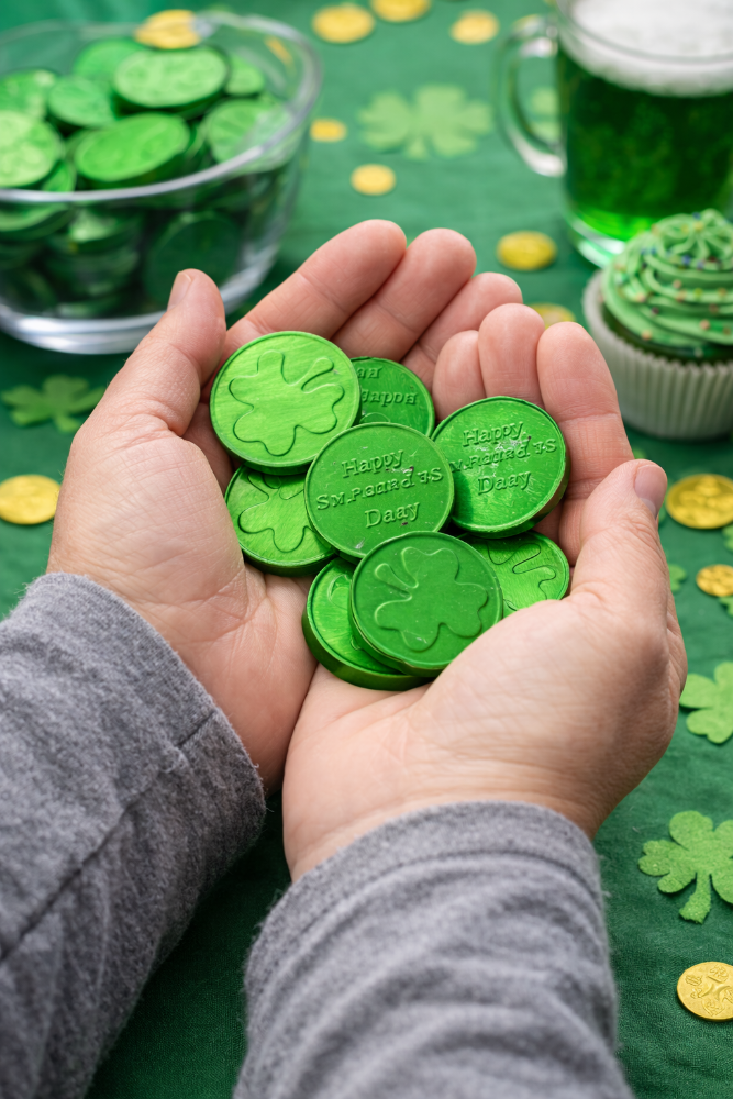 Green clover-shaped coins held in hands with St. Patrick's Day-themed table setting.