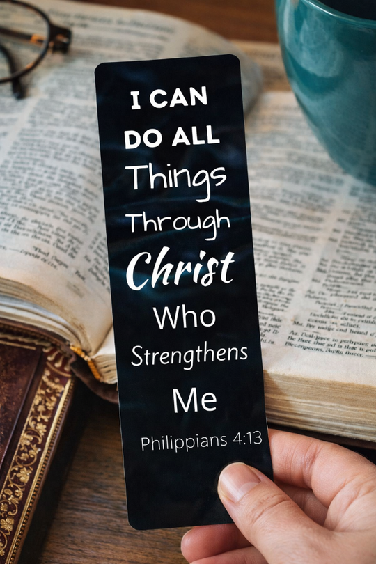 Black bookmark with inspirational quote held over an open book I can do all things through Christ