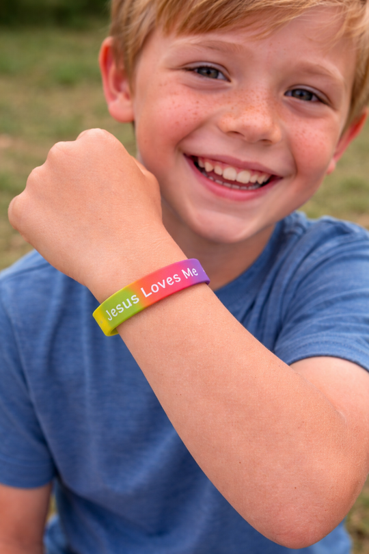 Child wearing a colorful 'Jesus Loves Me' bracelet outdoors