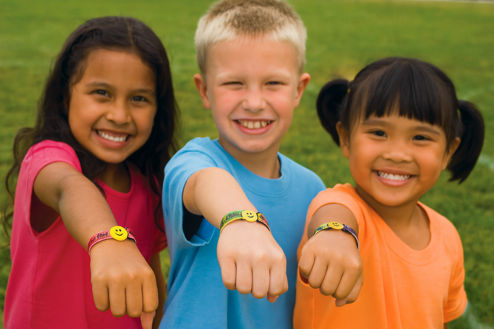 Three children with colorful bracelets showing their wrists outdoors.