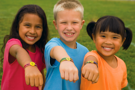 Three children with colorful bracelets showing their wrists outdoors.