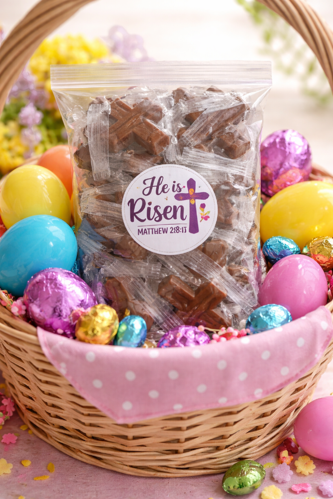 Easter basket with chocolate cross candies and colorful eggs on a pink background