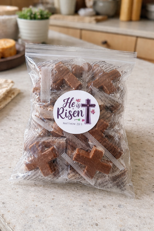 Bag of brown cross-shaped treats with a 'He is Risen' label on a kitchen counter.