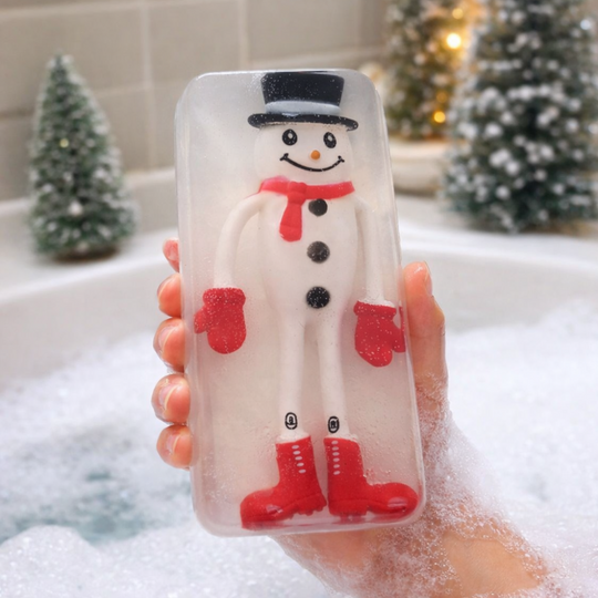 Bar of soap with snowman embedded inside of the design held in front of Christmas decorations. Christmas soap.