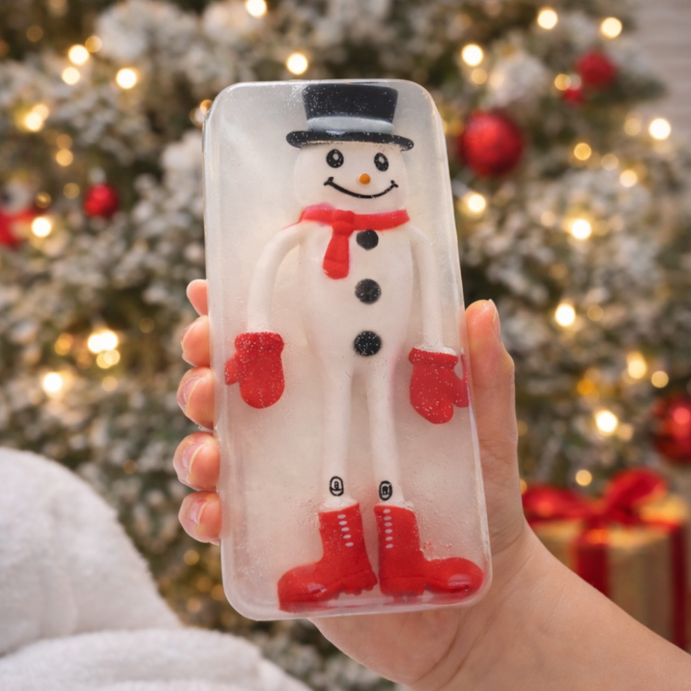 Christmas soap with a snowman design held in front of a decorated Christmas tree.