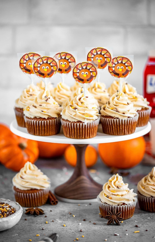 Cupcakes with pumpkin spice flavor on a stand with decorative toppers, surrounded by pumpkins and spices.
