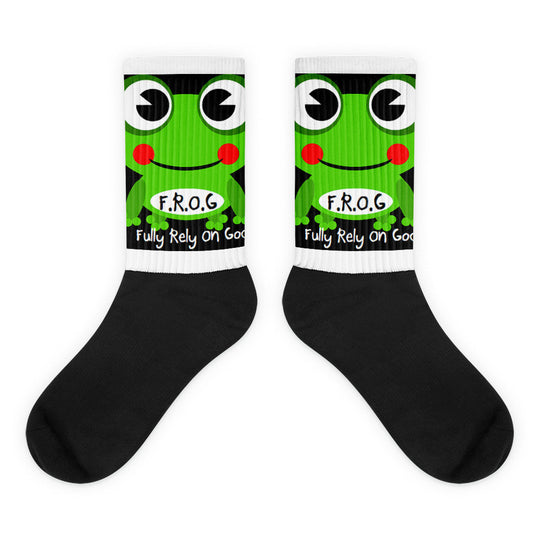 A pair of Christian crew socks on a white background featuring a smiling green frog with the text “F.R.O.G. – Fully Rely On God.” The socks have a white printed upper and a solid black foot, combining a fun design with a faith-based message.